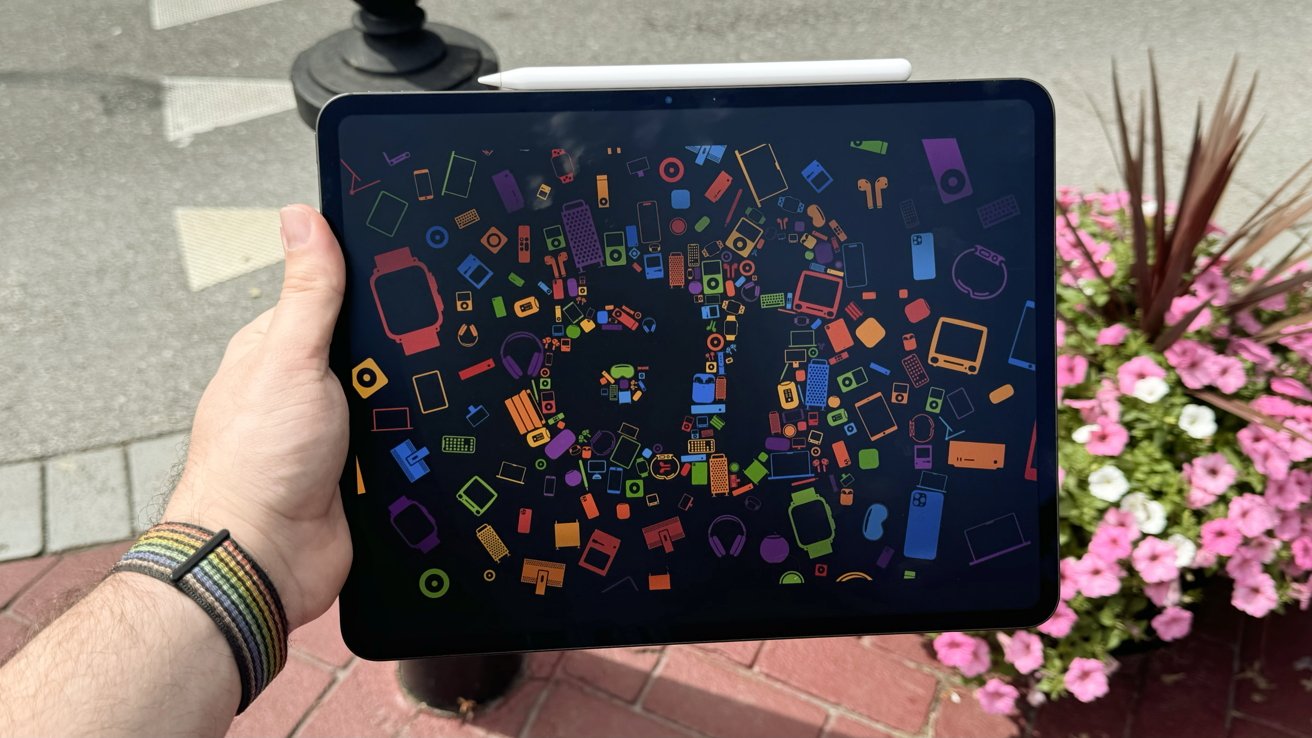 A hand holding the 13-inch iPad Pro with a colorful wallpaper showing the letters 'ai'