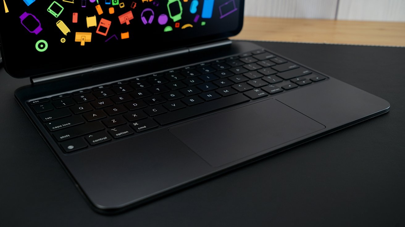 Laptop keyboard and touchpad on a dark surface, with a screen displaying colorful icons.