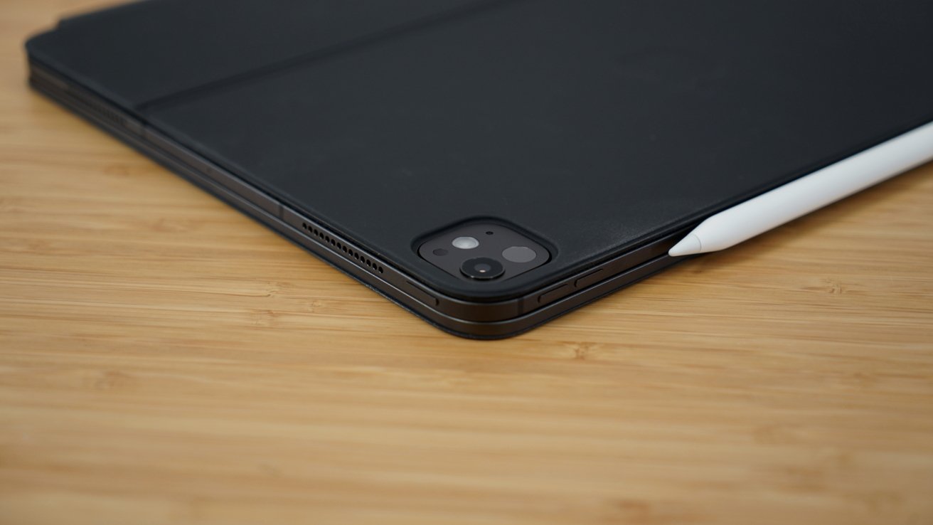 A tablet with a black cover and a stylus rests on a wooden surface; the camera lens is visible.