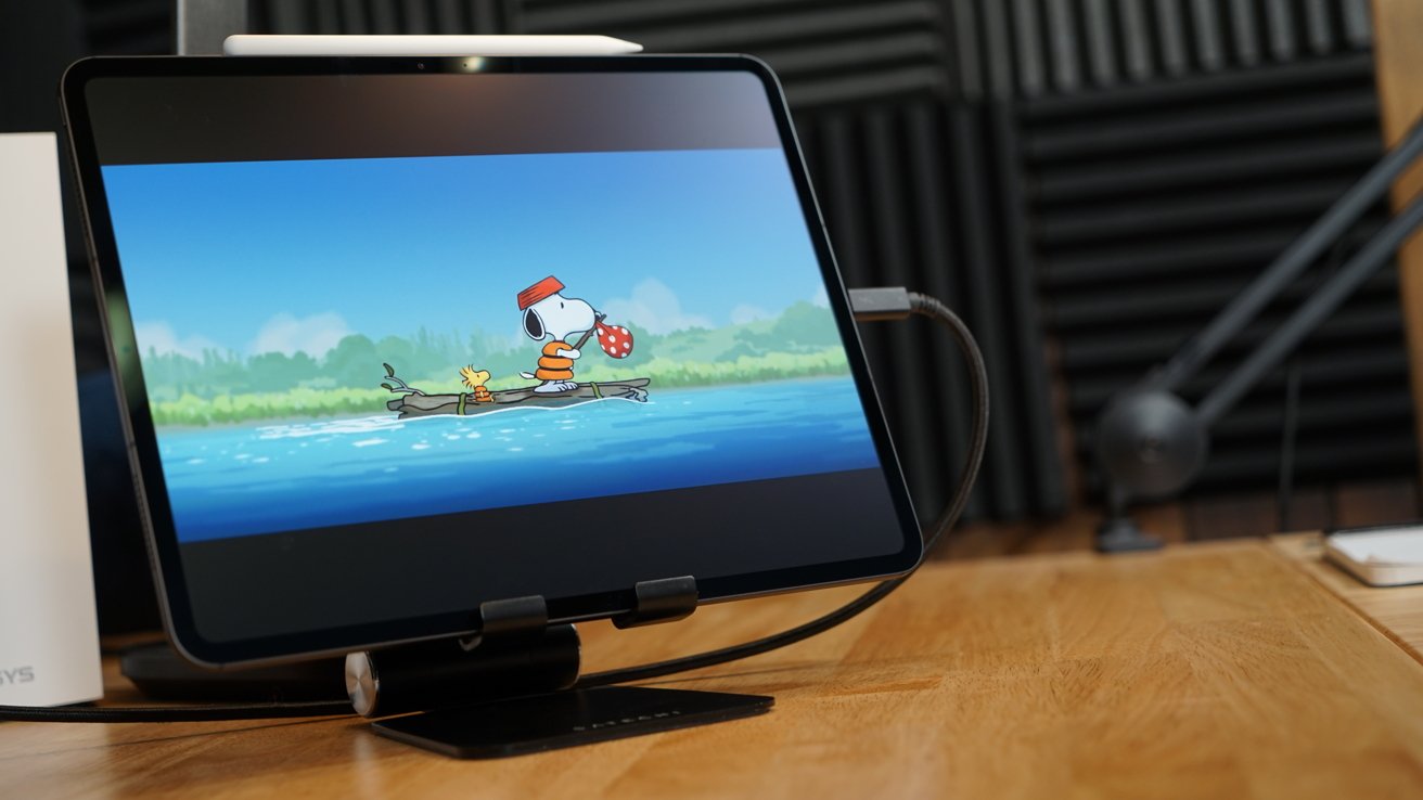 Tablet displaying cartoon characters Snoopy and Woodstock floating on a wooden raft on water, wearing adventure gear.