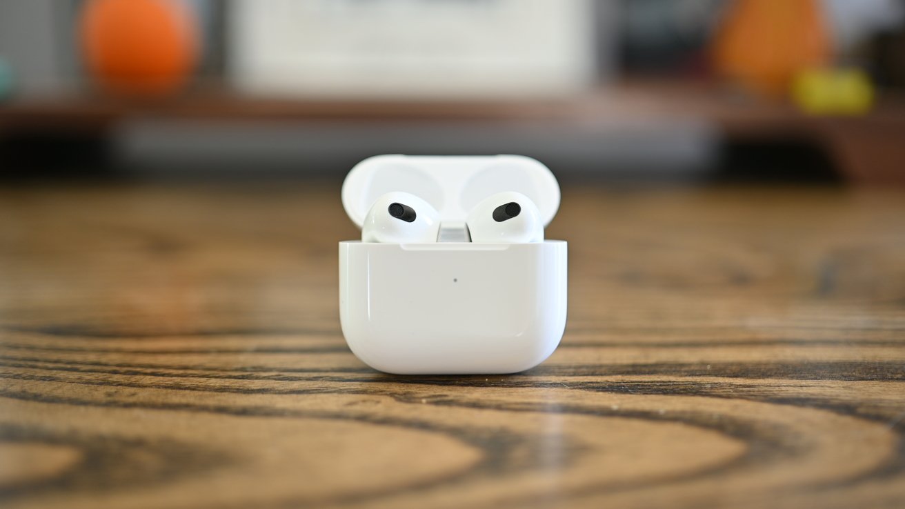 White wireless earbuds in an open charging case, placed on a wooden table with a blurred background.