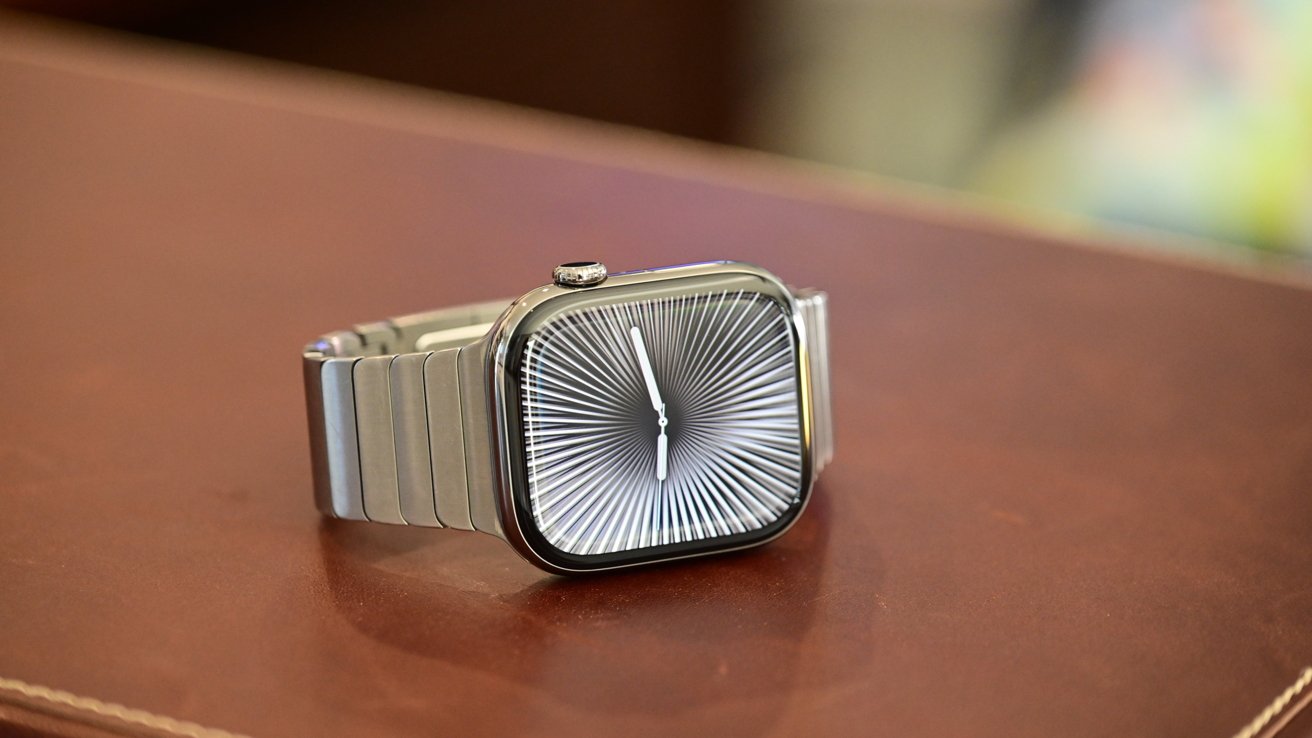 A metal wristwatch with a radial pattern on the face lying on a brown surface.