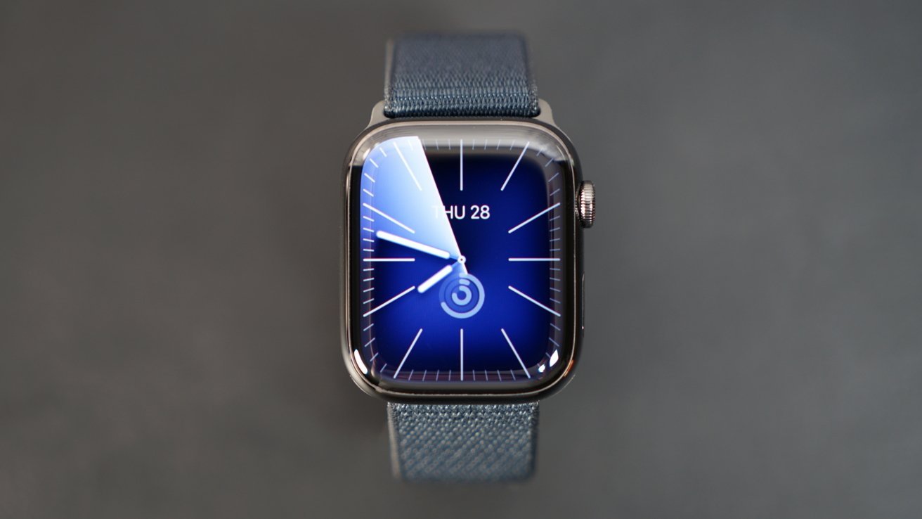 Apple Watch Series 9 smartwatch with a blue watch face displaying time, on a gray background.