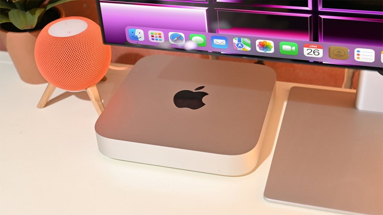 Apple Mac mini on a desk next to a HomePod mini speaker and a computer monitor with colorful icons.