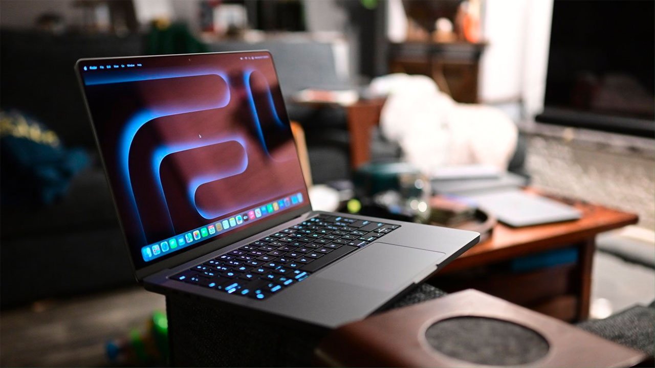 MacBook Pro laptop with an illuminated keyboard on a wooden surface, with a blurred room background.