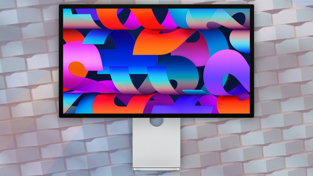 Computer monitor displaying colorful abstract shapes with a gradient background, mounted on a stand against a white brick wall.