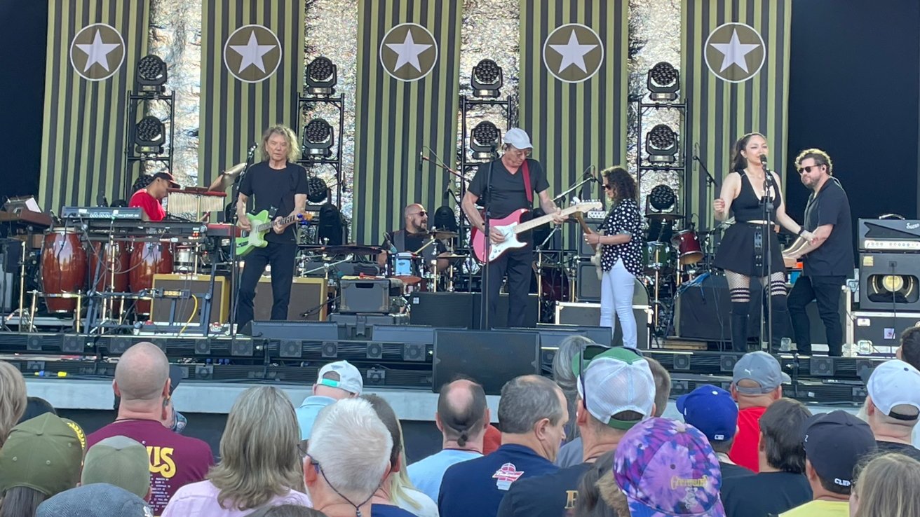 Band playing onstage, with some onlookers at the bottom of the stage area