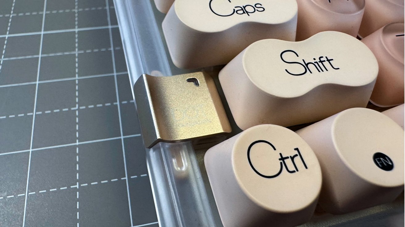 Close-up view of beige computer keyboard keys labeled Caps, Shift, Ctrl, and FN with a metal tab on the side, against a gridded background.