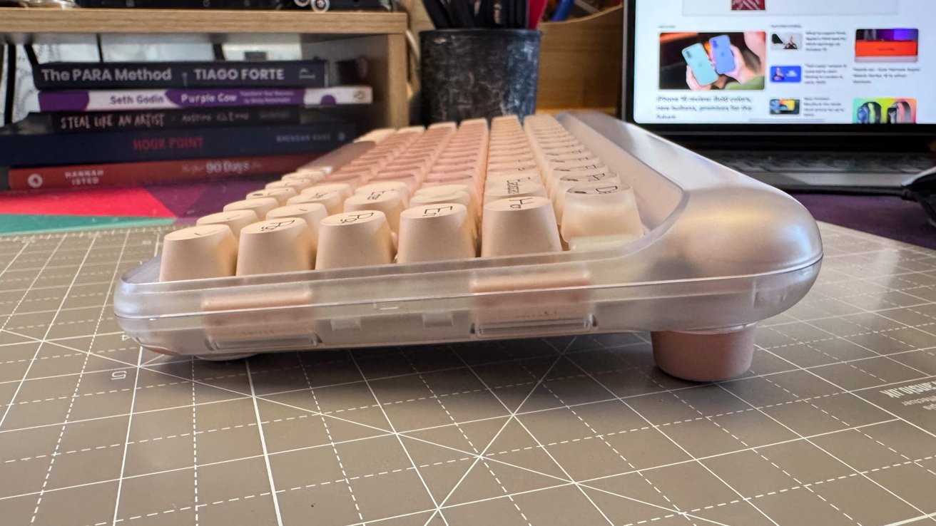 Side view of a retro-style mechanical keyboard on a cutting mat, with books and a laptop in the background.