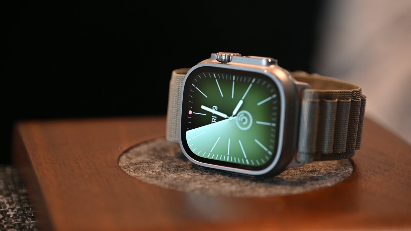 A smartwatch with a green dial displaying the time and date, placed on a wooden surface.