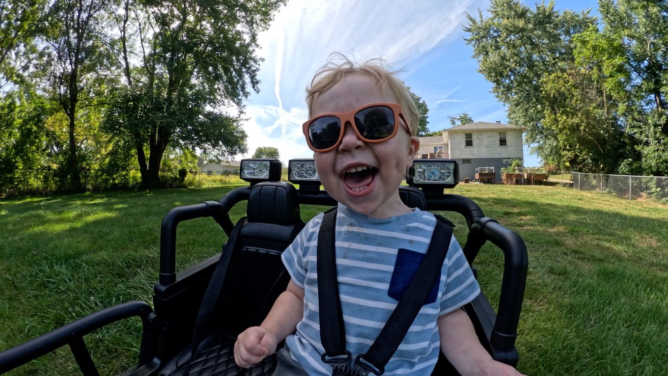 Example of a POV shot of a toddler driving a toy Jeep in the grass wearing sunglasses