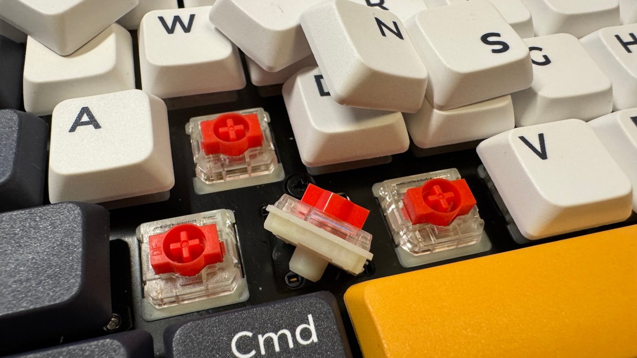 Close-up of a mechanical keyboard with some keys removed, revealing red switches beneath.