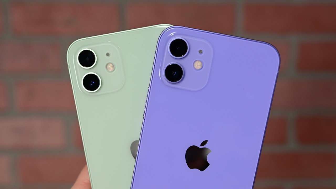 Two iPhones, one light green and one purple, showing their backs with dual cameras and Apple logos, against a blurred brick wall background.