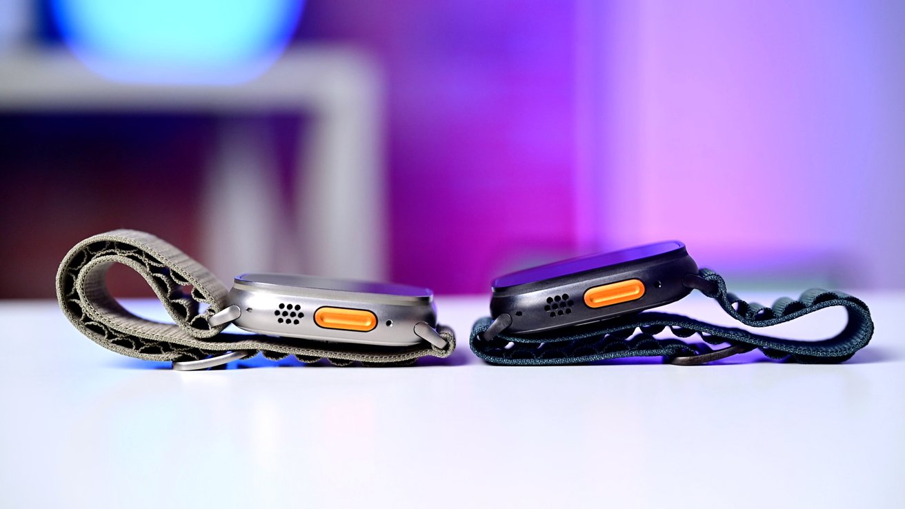 Two smartwatches with orange side buttons on a white surface, featuring rugged woven bands, against a blurred purple background.