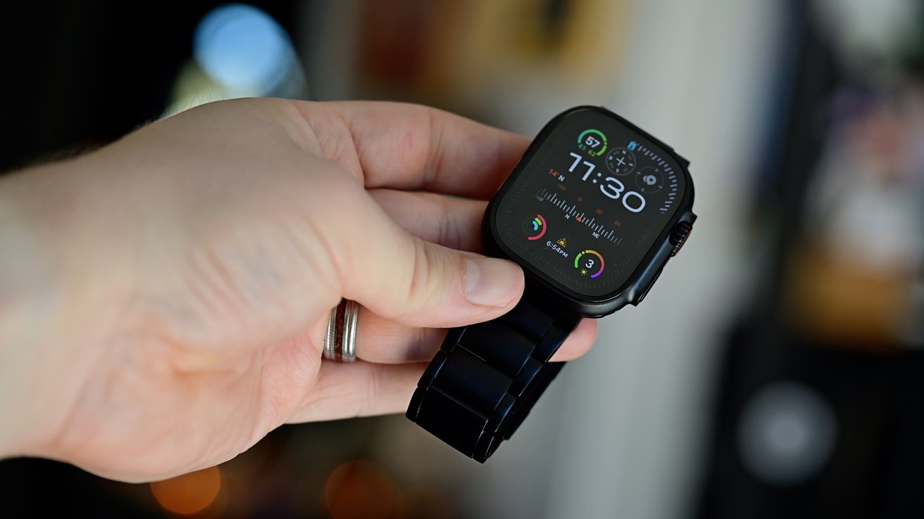 A hand holding a black Apple Watch Ultra 2 with a colorful watch face