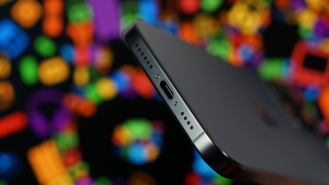 Close-up of the edge of a smartphone showing a USB-C charging port and speaker holes, with a colorful, blurred background.