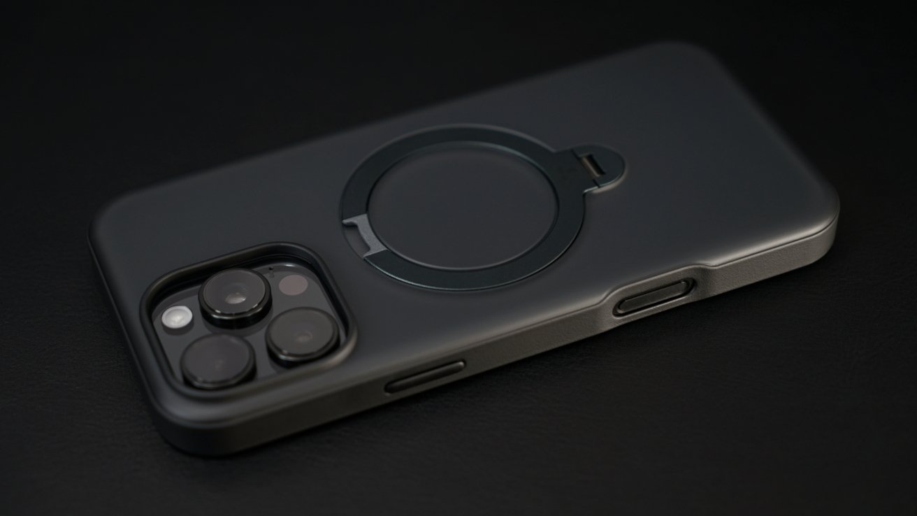 Dark grey smartphone with a camera module showing three lenses and a circular magnetic ring on the back case, resting on a dark surface.