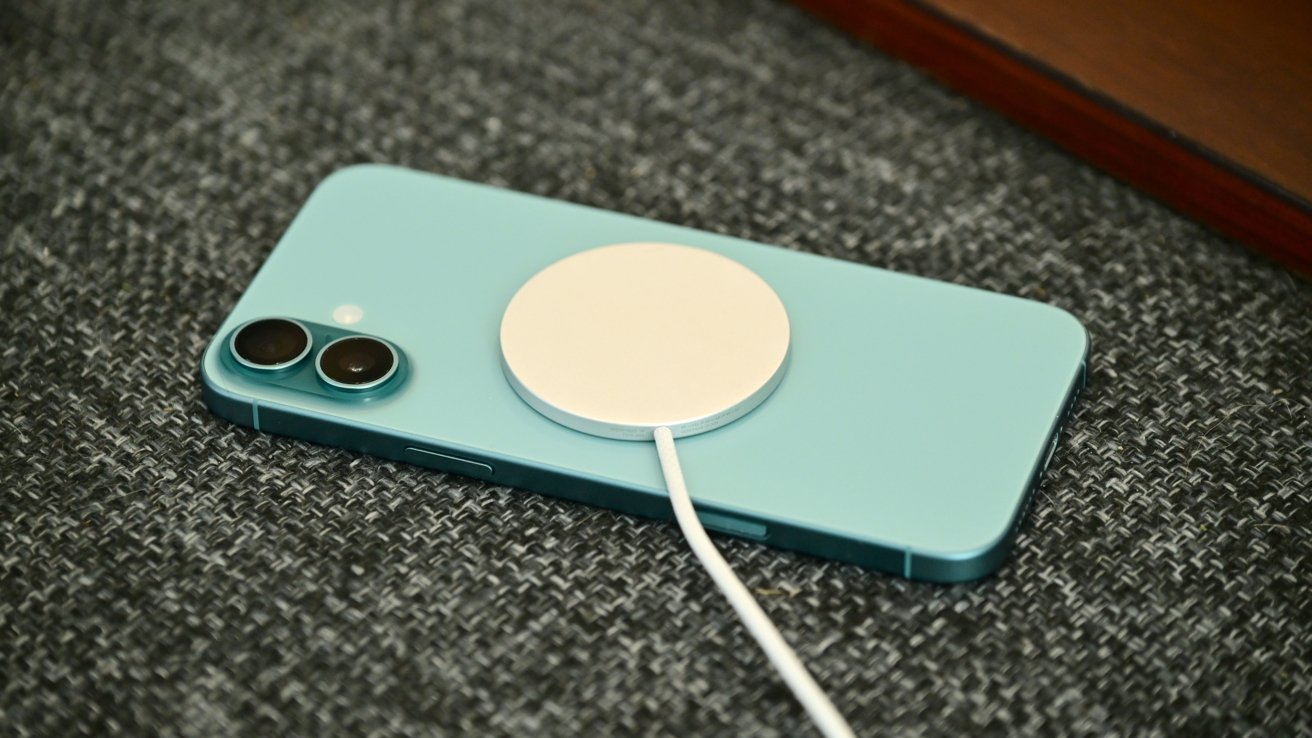 A blue smartphone lies face down on a textured surface with a white circular wireless charger attached.