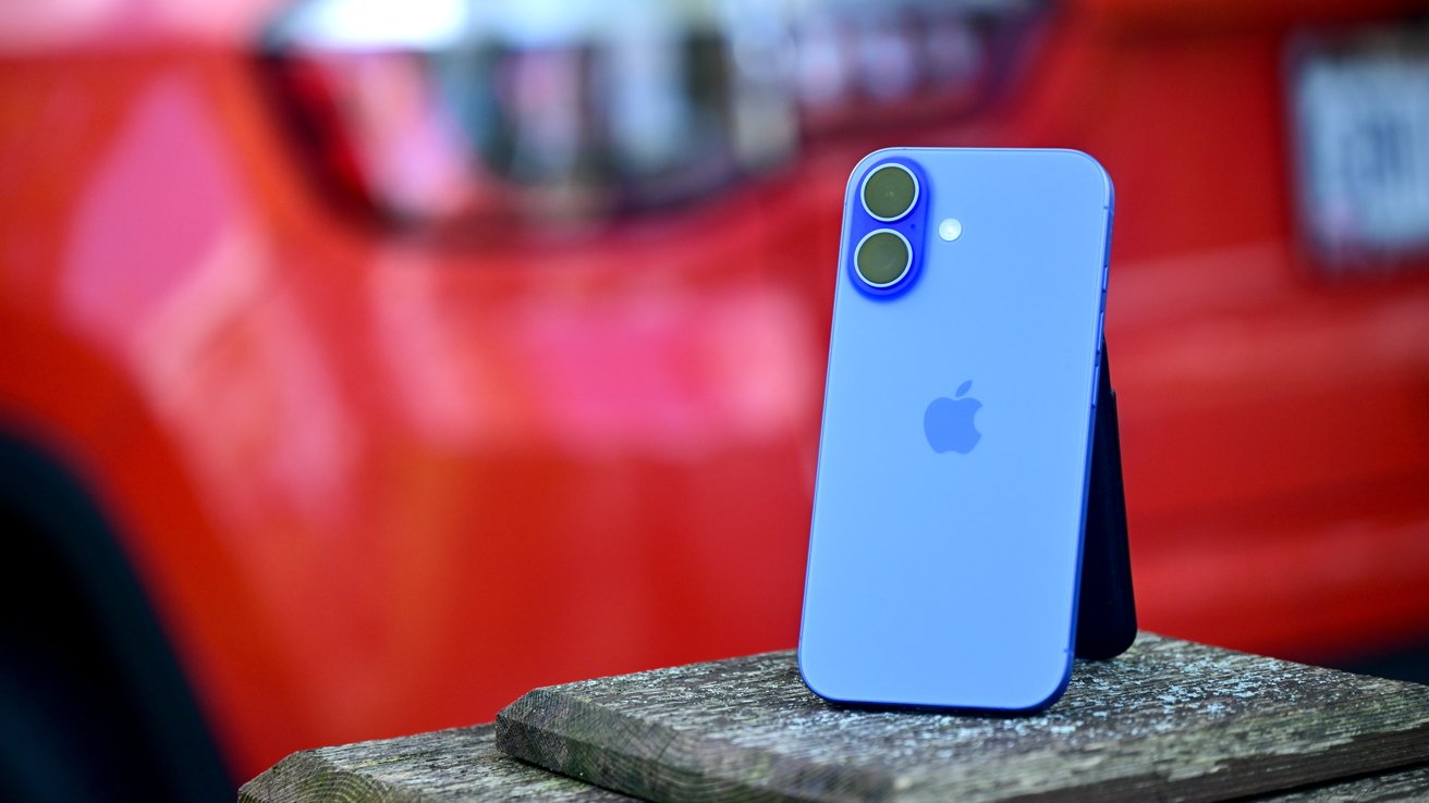 A blue smartphone with dual cameras on a wooden surface, blurred red background.