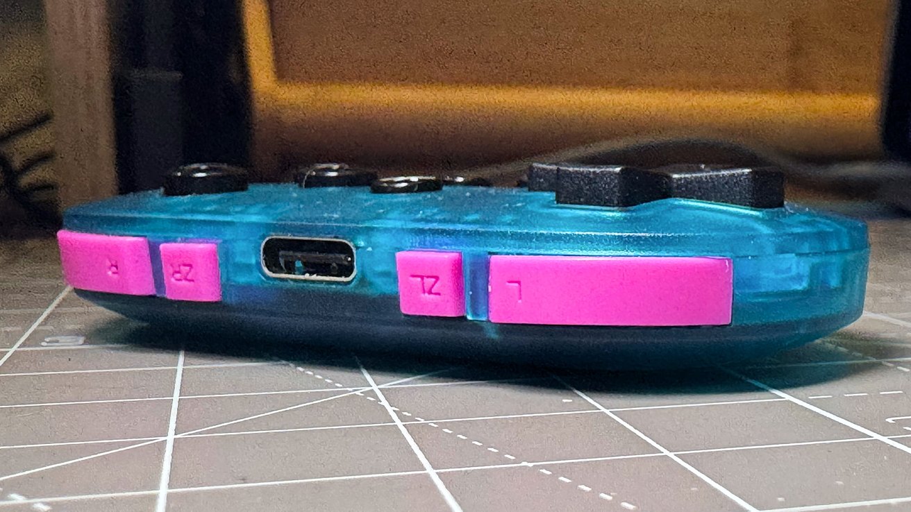 Blue and pink game controller laying on a desk, showing buttons and a charging port.