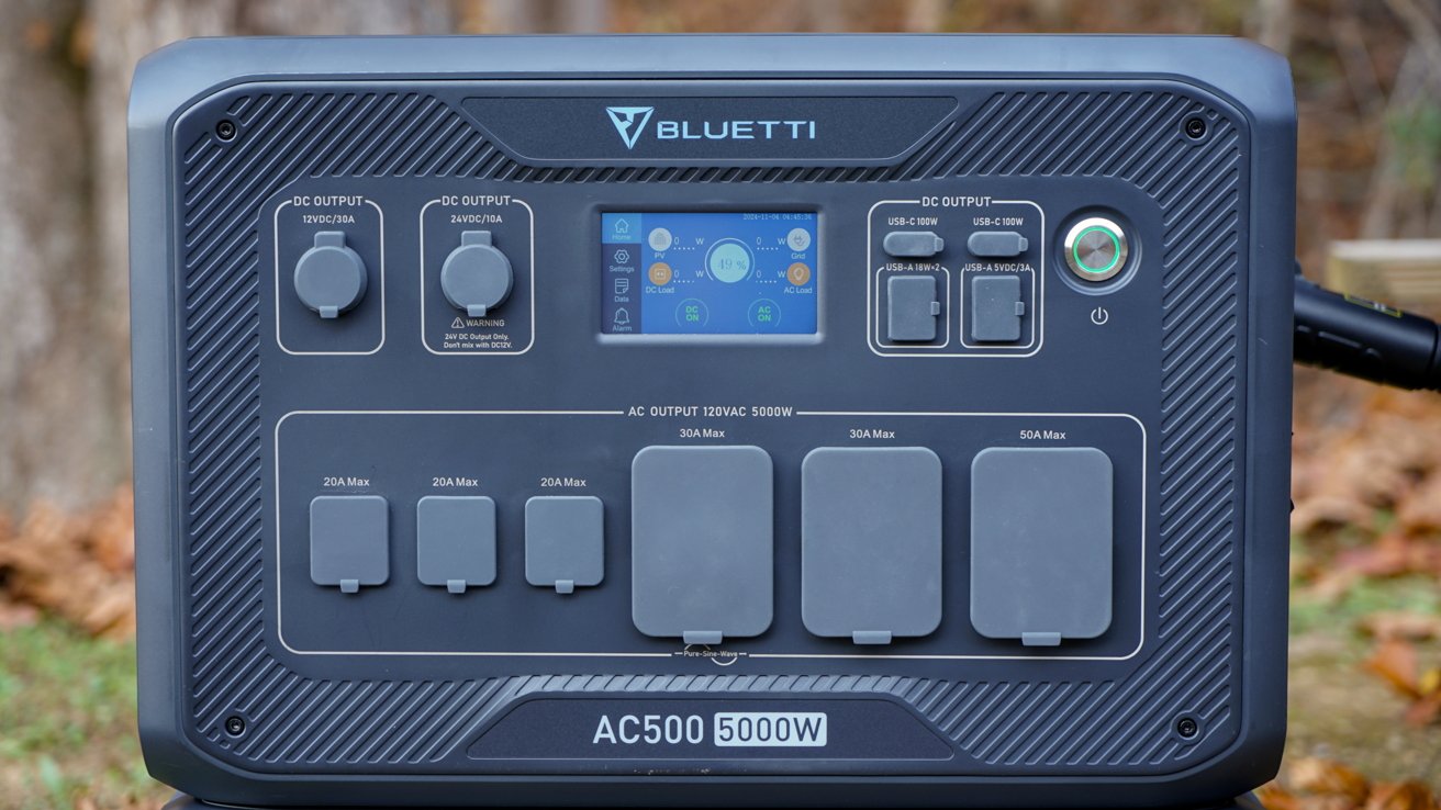 Portable power station with multiple outlets, a central display screen, and control knobs, set in an outdoor background.