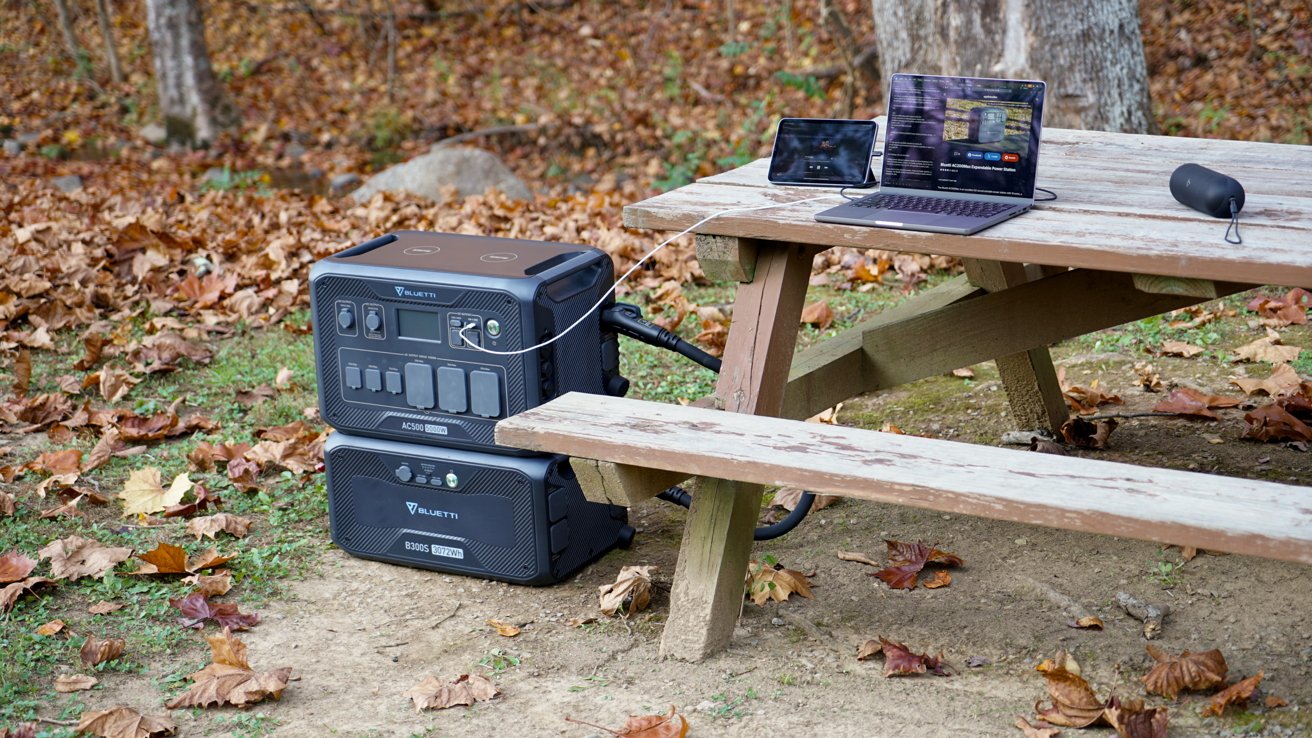 Portable power station and equipment set up on a picnic table amidst autumn leaves in a wooded area.