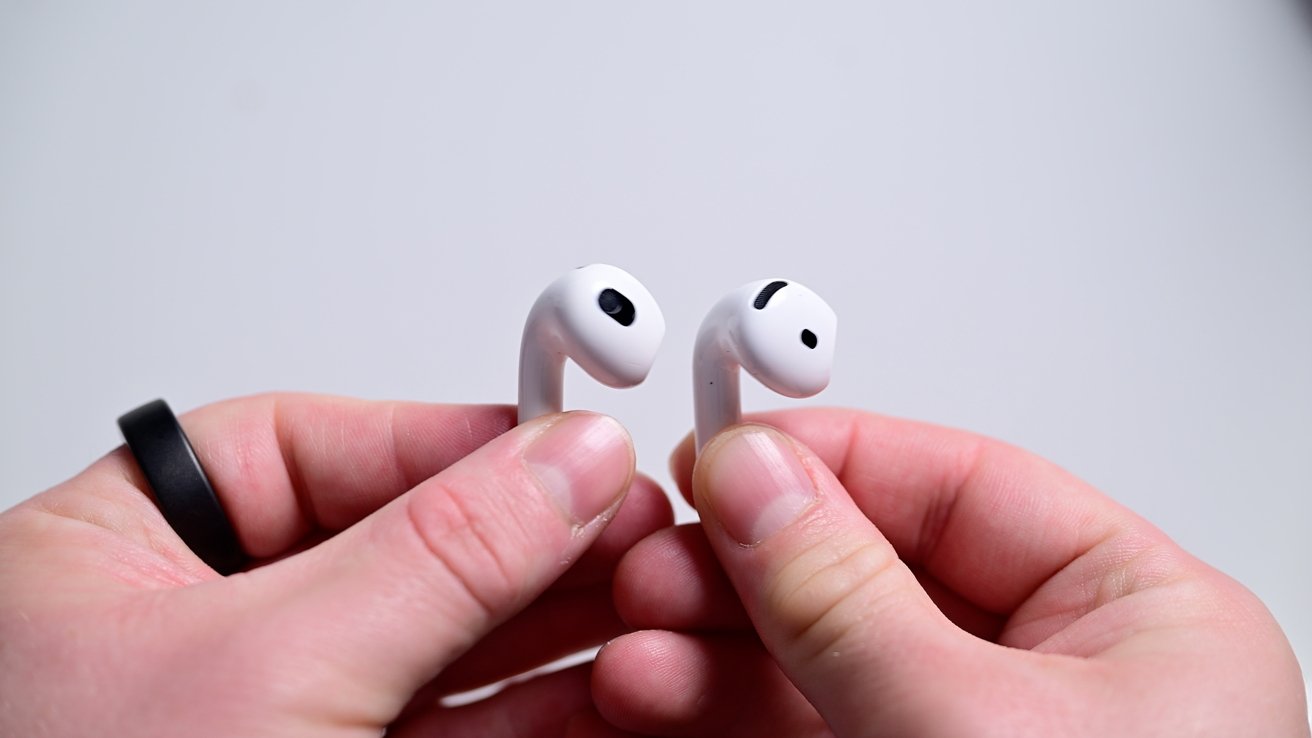 Two hands holding a pair of white wireless earbuds against a plain background.