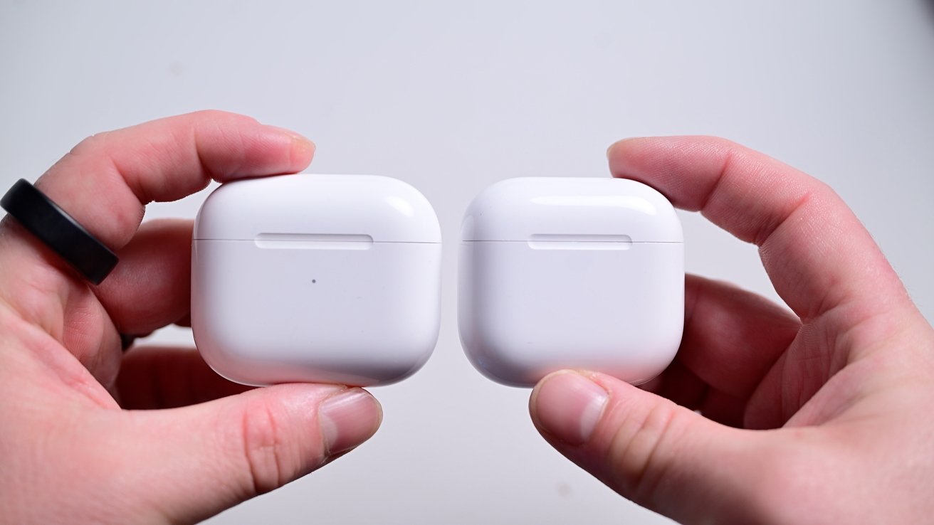 Two hands holding white wireless earbud cases side by side against a plain background.