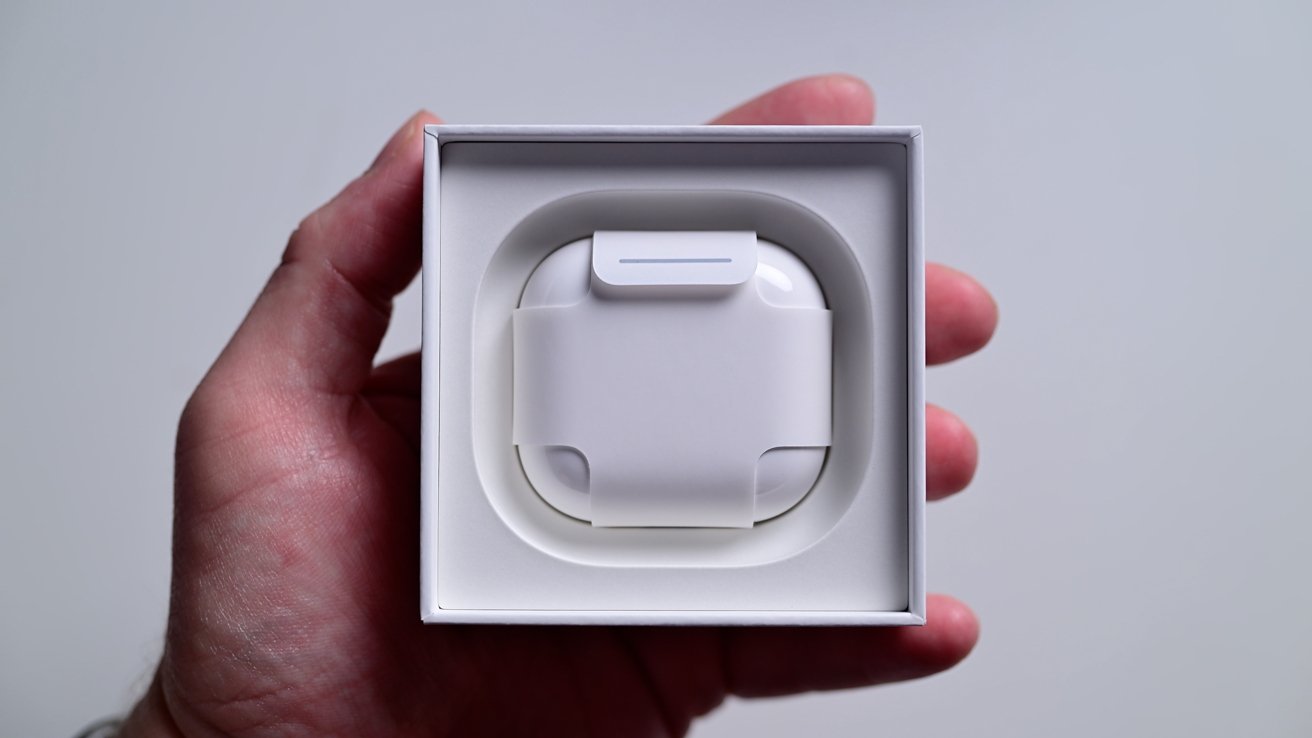 Hand holding an open box containing a set of white wireless earphones in a compact charging case.