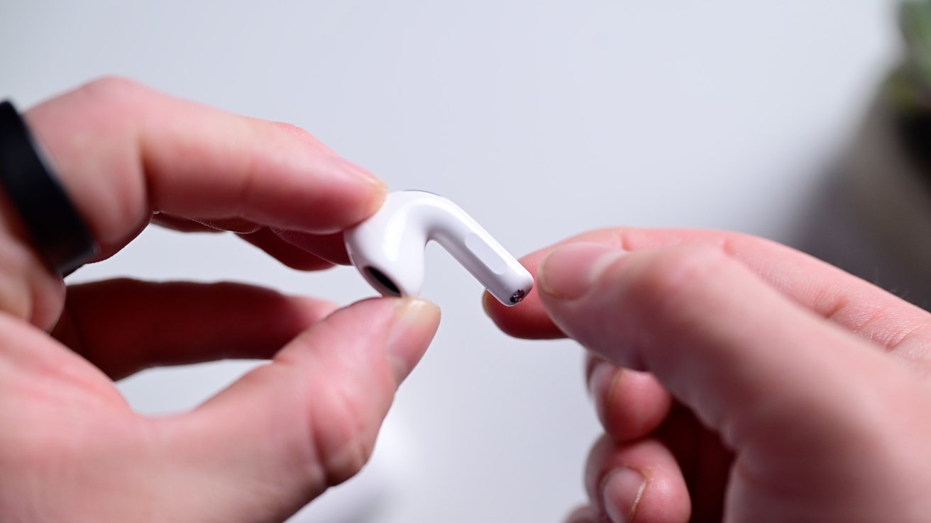 Hands holding a small, white, wireless earbud against a plain background.