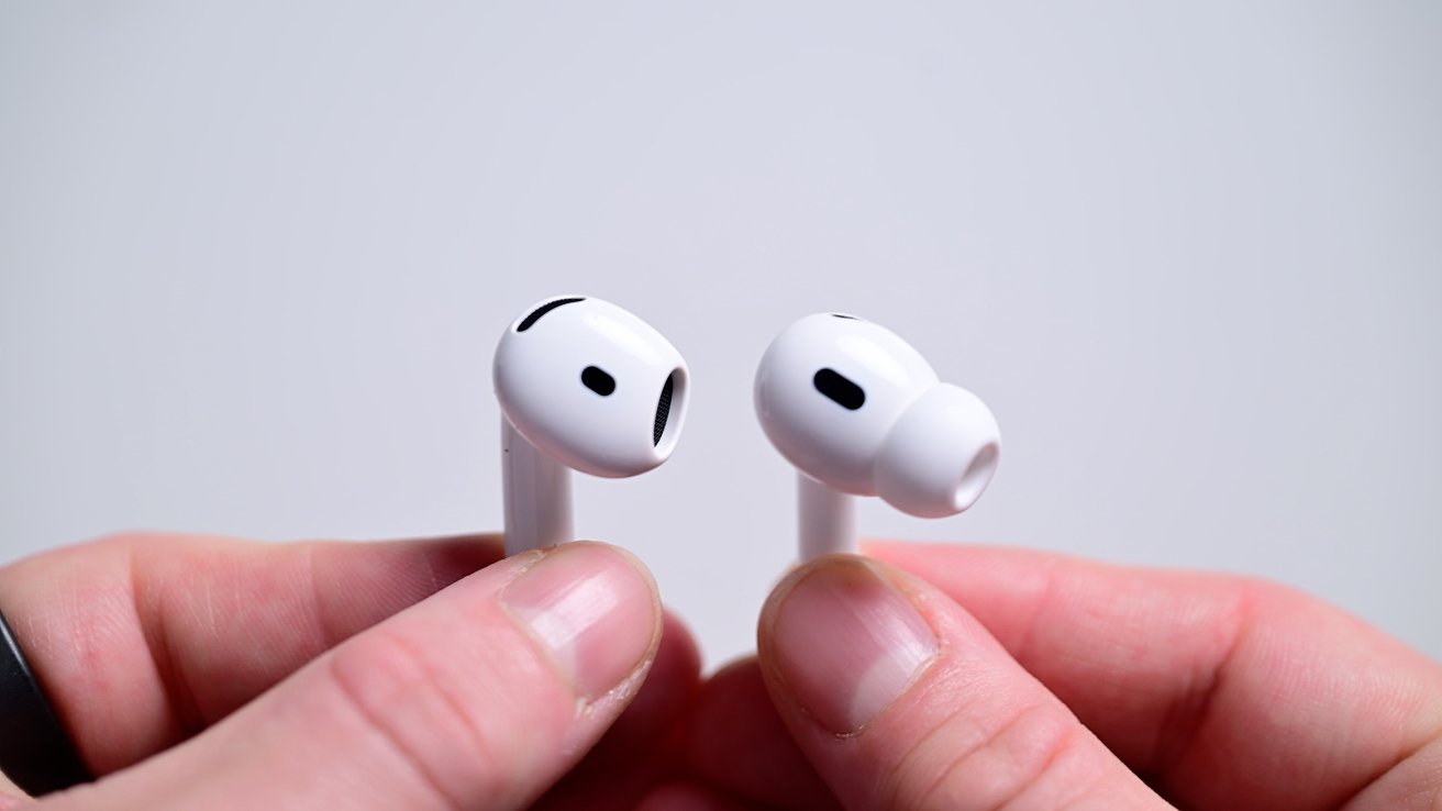 Close-up of hands holding a pair of white wireless earbuds with silicone tips, on a neutral background.