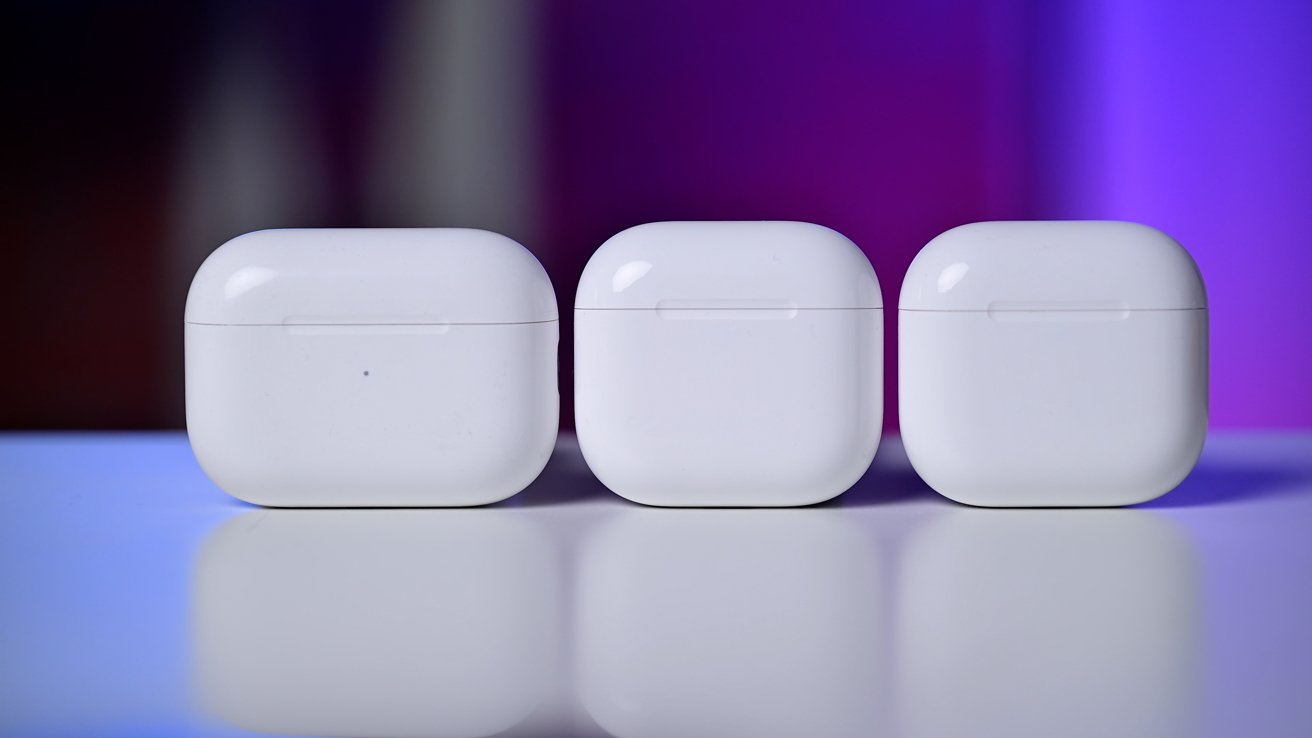 Two white wireless earbuds with black accents are held by fingers against a plain background.