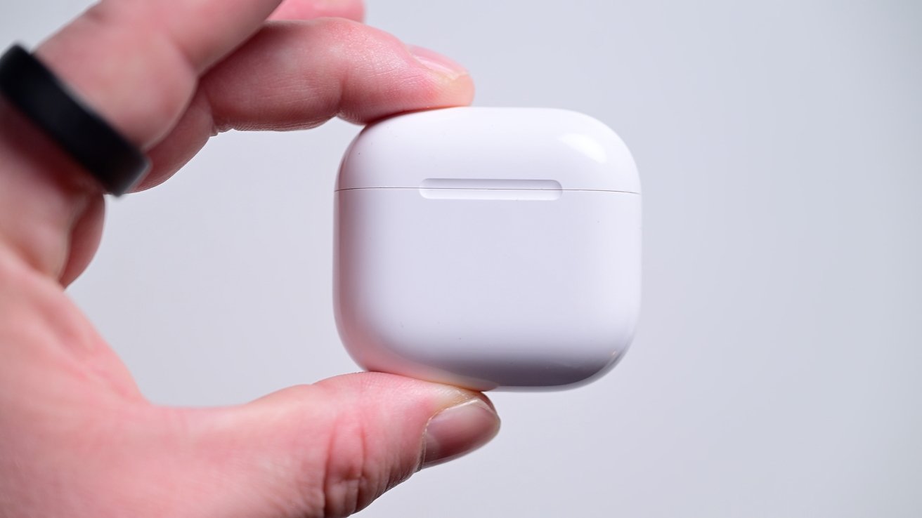 Hand holding a white wireless earbud case with a smooth finish against a light gray background.