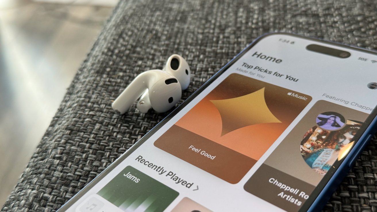 Smartphone displaying a music app and wireless earbuds resting on a textured gray surface.