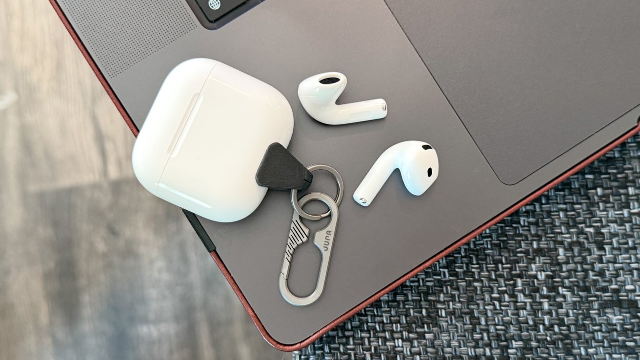 White wireless earbuds and charging case with a keyring lying on a closed laptop on a woven surface.