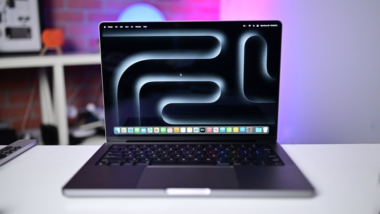 A laptop with a glowing abstract pattern on the screen sits on a desk, with a blurred background featuring colorful lighting.