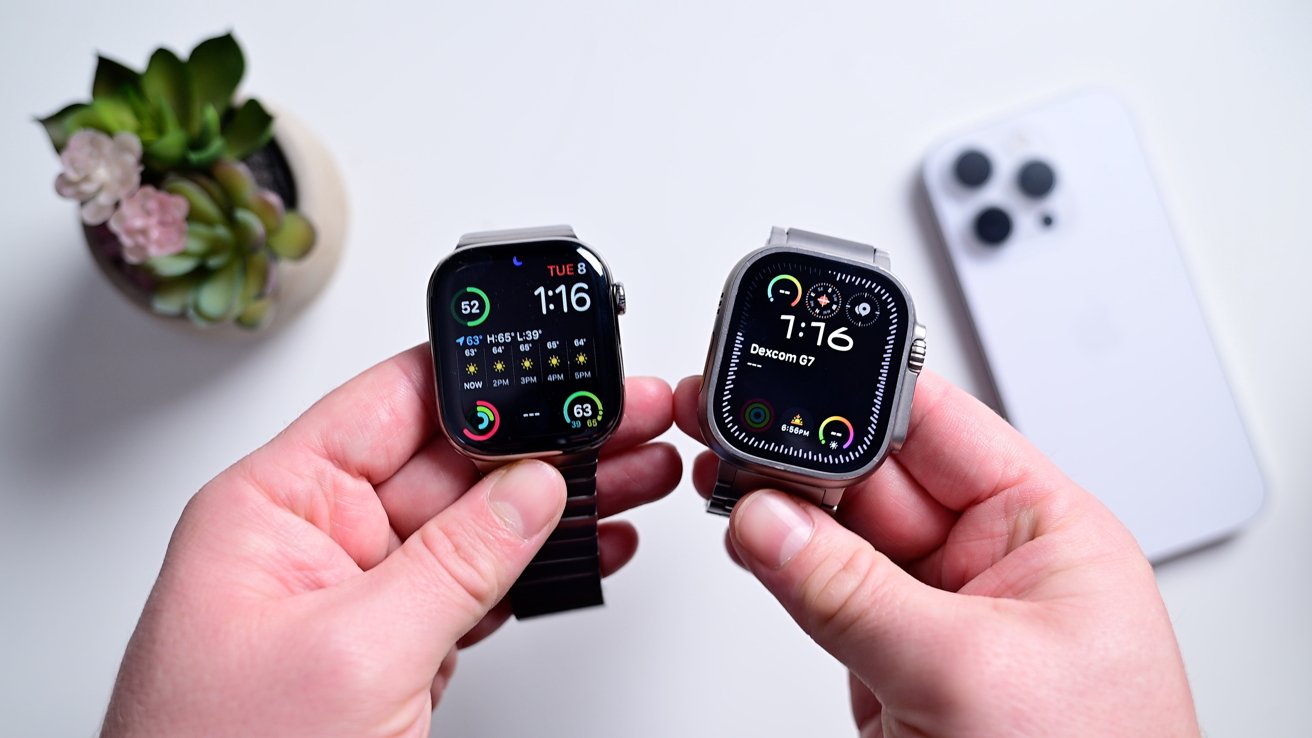 Two hands hold smartwatches with colorful displays, in front of a blurred background featuring a small plant and a smartphone.