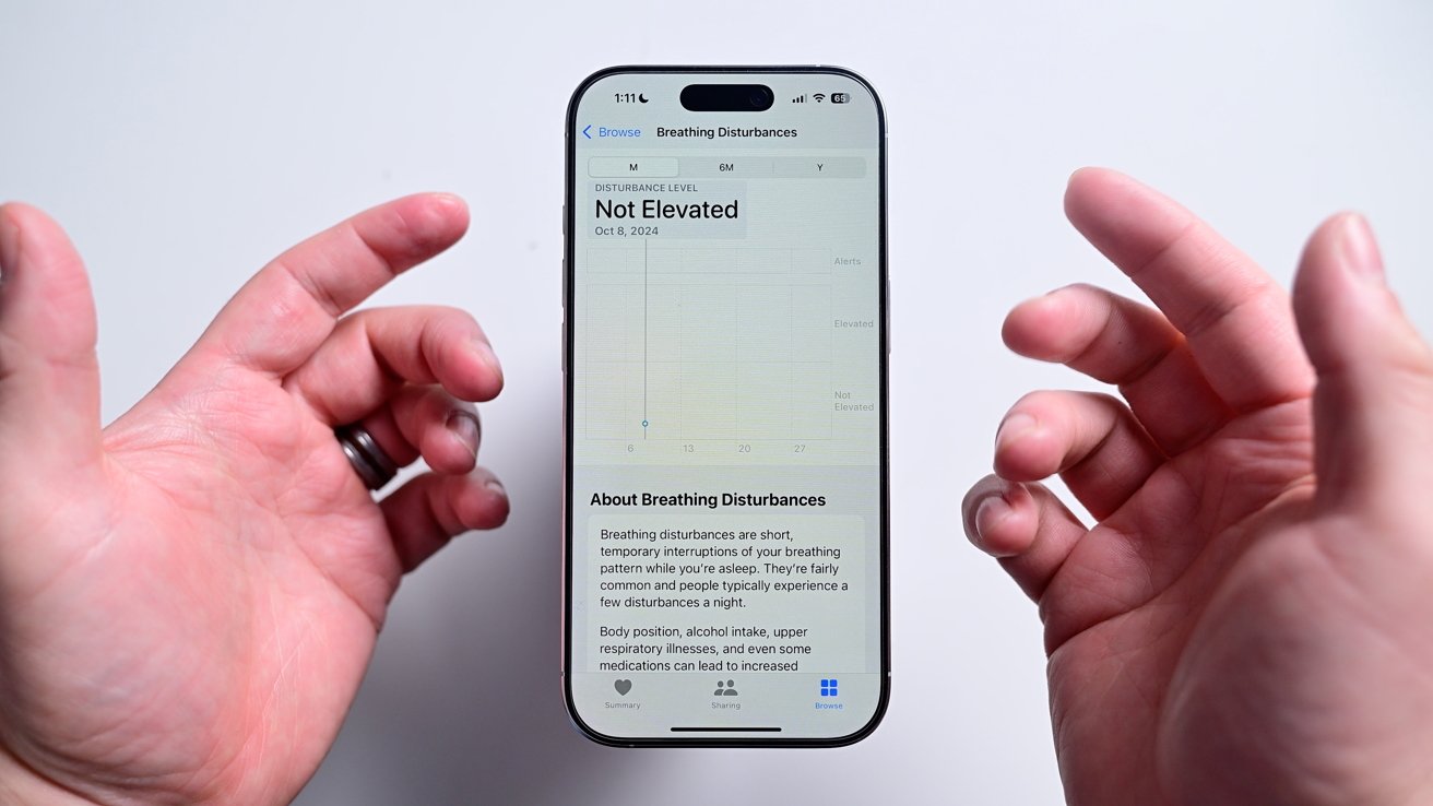 Hands holding a smartphone displaying a screen about breathing disturbances, with text mentioning 'Not Elevated' and information on breathing patterns and related factors.