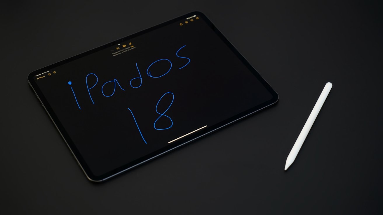 Tablet screen displaying handwritten 'iPadOS 18' in blue, accompanied by a white stylus on a dark surface.