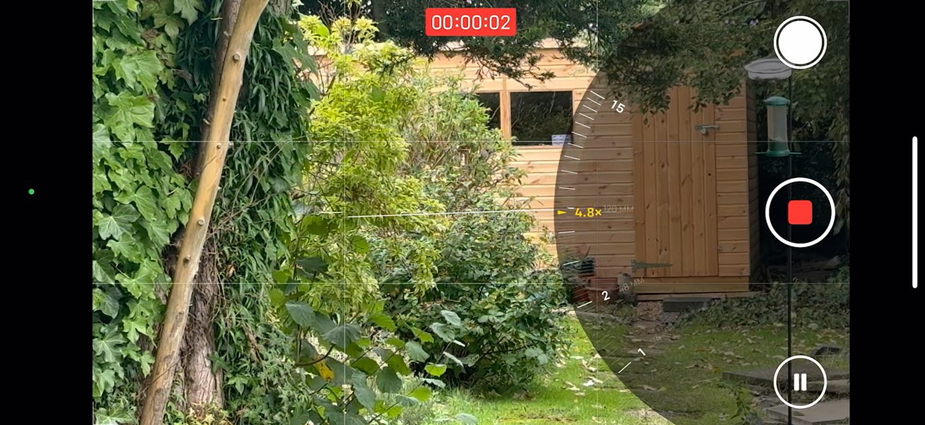 Garden scene with greenery, a wooden shed, and a bird feeder. Camera interface overlays show recording and zooming features.