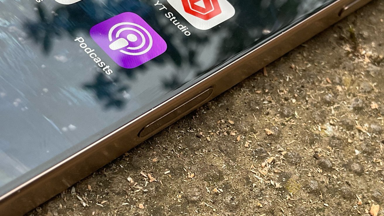 Smartphone with podcast and studio app icons on screen, lying on a textured, earthy surface.