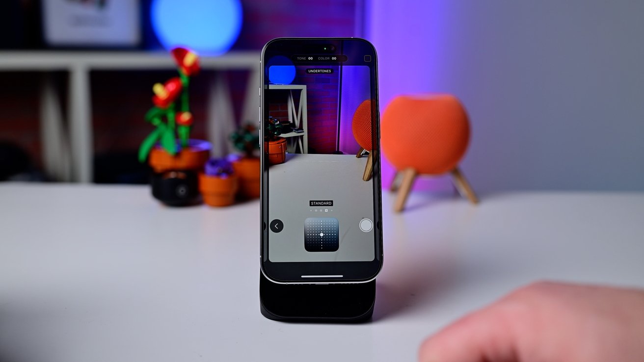 Smartphone on table with camera app open, capturing potted plants and colorful objects in blurred background.