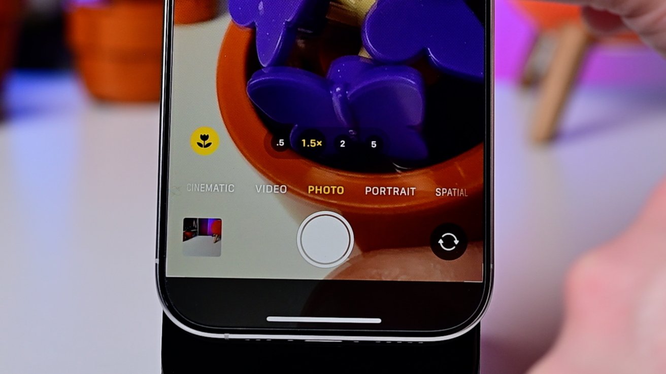 Smartphone camera interface displaying a photo mode, focused on a close-up of purple butterfly shapes in an orange pot.