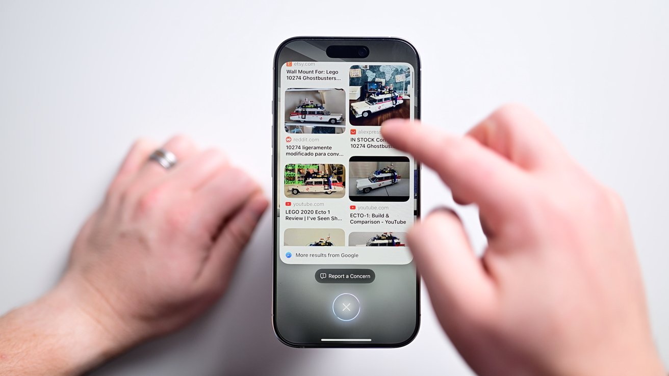 Two hands interact with a smartphone displaying search results for Lego Ghostbusters sets on a white background.