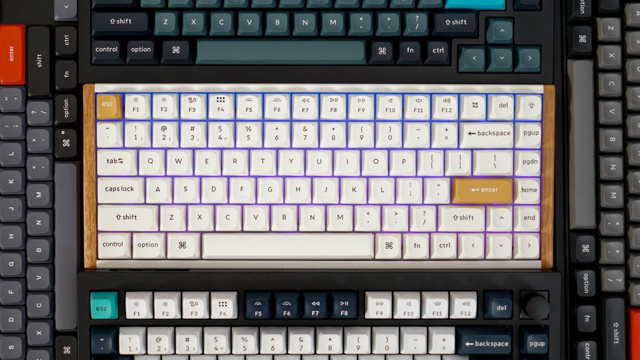 Stacked mechanical keyboards with varying keycap colors, featuring white, teal, and gray layouts, with wooden accents on one keyboard.