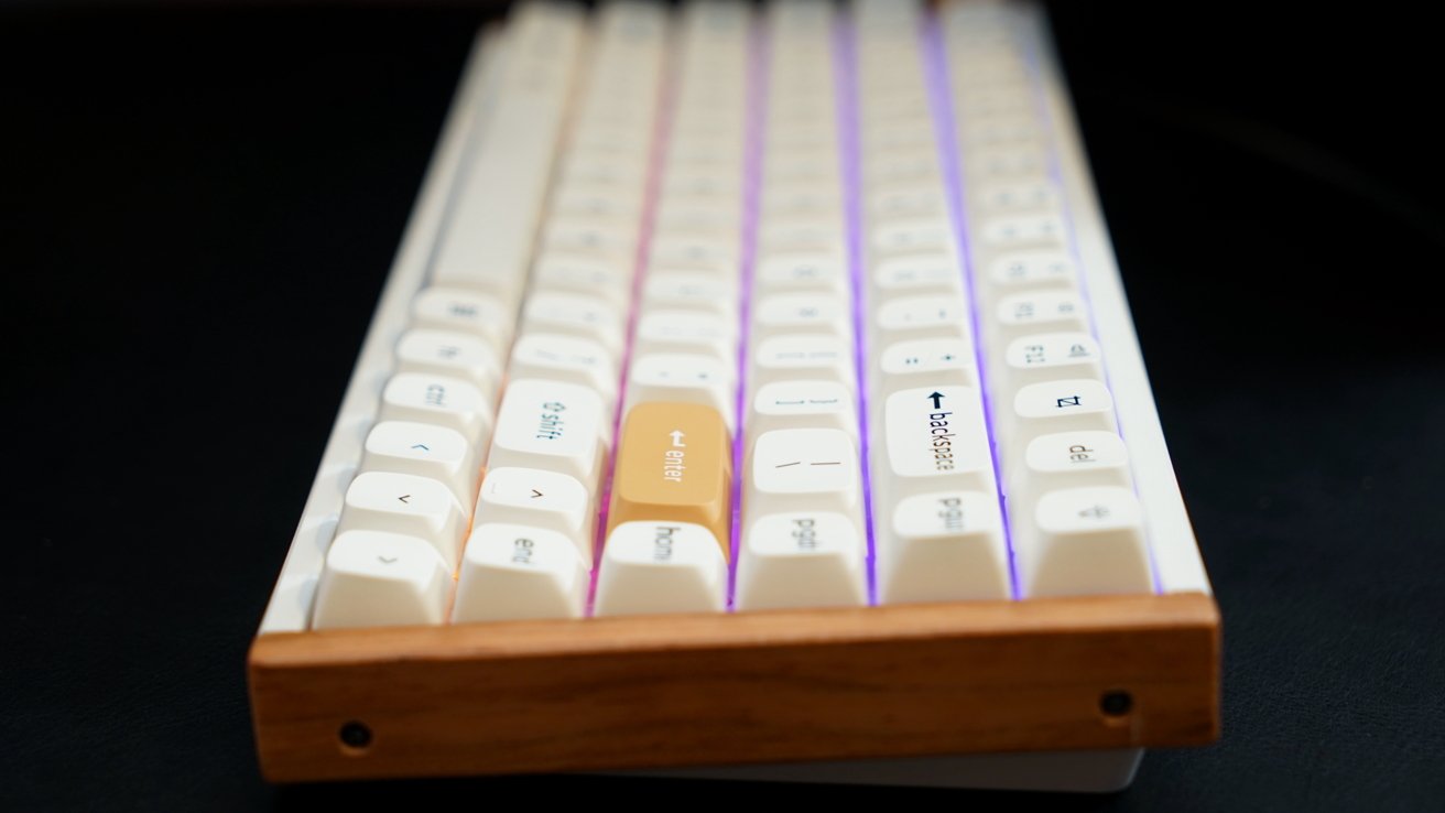 White mechanical keyboard with purple backlighting, featuring a wooden wrist rest and an orange keycap among the white keys.