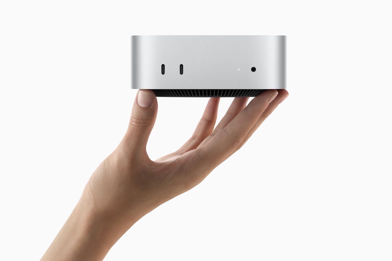 A hand holds a small, metallic, rectangular device with two USB-C ports, a dot, and a circular hole on the front.