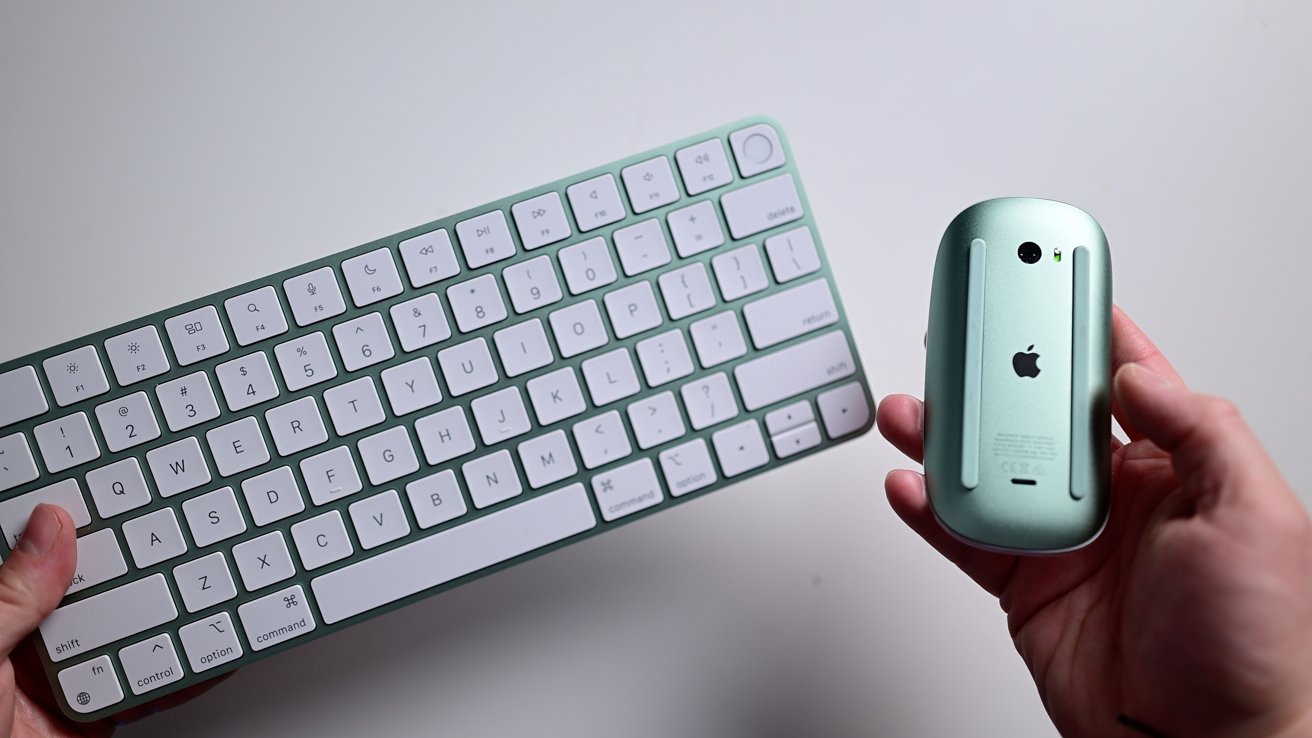 Hands holding a green wireless keyboard and a green wireless mouse with an apple logo on a white background.