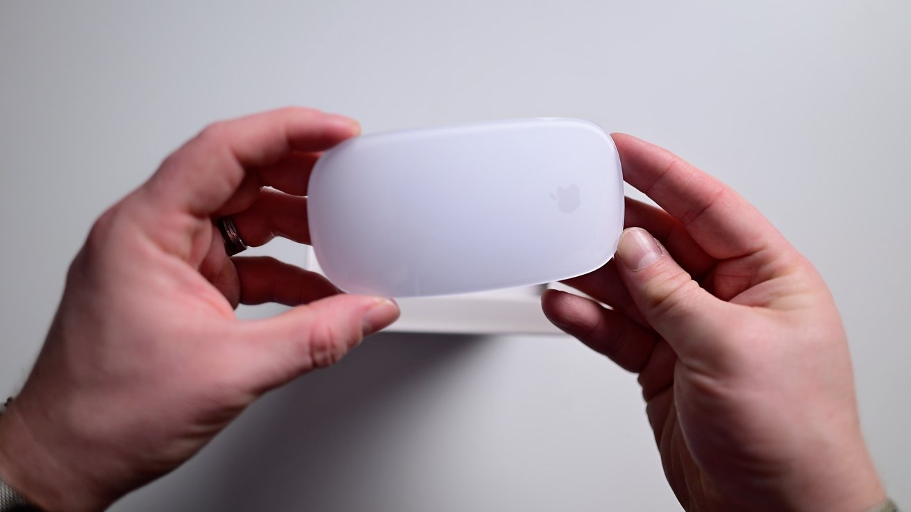 Hands holding a sleek white wireless mouse with a slightly transparent design, visible logo, and smooth surface.