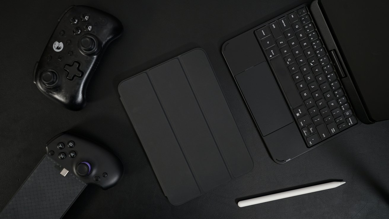 Black gaming controllers, a tablet with keyboard, and a stylus on a dark surface.